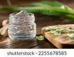 Small photo of Transparent glass jar of aloe vera gel, sliced aloe leaves on a cutting board. Aloe vera plant on background. Natural cosmetic and medicinal remedy.
