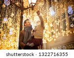 smiling girl in the arms of the father in a brown coat pulls his hands to the lights on the decorated street of the city center