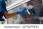 Small photo of Male professional cleaning service worker in overalls cleans the windows and shop windows of a store with special equipment