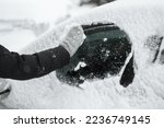 Cleaning snow from the side window of the car with a glove during a snowfall, the driver does not have a car brush. Snow cyclone, cleans snow from the car. Road safety concept.