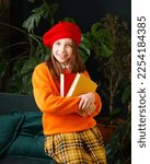 Small photo of Glad Schoolgirl holds two books. Girl wears bright outfit and woolen red beret. Concept of bookworm, bibliophile and International Children's Book Day