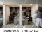 Small photo of Two diverse businessmen working at desks in cubicles with blurred colleagues walking around a busy office