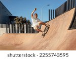 Small photo of Side view portrait of young man riding skateboard and doing tricks on ramp at skatepark outdoors