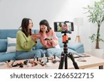 Small photo of Two girls influencers in the living room at home putting on makeup and recording themselves on video with a mobile phone on a tripod for social networks