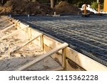 Small photo of Iron fittings on a wooden formwork with laid pipes are the basis for pouring the foundation of the house with a concrete slab. Construction of cottages, design, engineering communications.