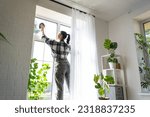 Woman manually washes the window of the house with a rag with spray cleaner and mop inside the interior with white curtains. Restoring order and cleanliness in the spring, cleaning servise
