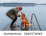 Handsome caucasian girl caress brown Nova Scotia Duck Tolling Retriever. Woman with pet sitting on pier on lake and look into each other eyes. Female travelling with dog. Selective focus. Dog loyalty.