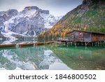 Amazing view of the famous Braies Lake in Italy, with wooden house in the middle and row boats docked. Amazing water reflections on the lake's surface. Pines, fall foliage and mountains.