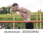 Attractive Caucasian young brunette man in sportswear doing push-ups on the bars at a playground on a warm summer day. Sports, workout, health, body care.