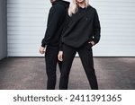 Man and woman wear black hoodies.  A fashion template for print and branding on hoodie. trendy couple on the street wearing casual apparel with no face visible. No logo sweater and pullover with hood.