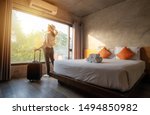 Portrait of tourist woman standing nearly window, looking to beautiful view with her luggage in hotel bedroom after check-in. Conceptual of travel and vacation.