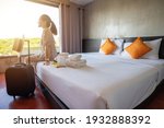 Tourist woman sitting on bed nearly window, looking to beautiful view with her luggage in hotel bedroom after check-in. Conceptual of travel and accommodation.