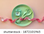 Creative flat lay composition with plate, alarm clock, spoon, fork and measuring tape on pink background. Intermittent fasting, ketogenic, diet concept.  Flat lay, copy space.
