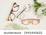 Small photo of several trendy stylish glasses and flowers on a beige background place copy top view, optics, shop of glasses and frames concept