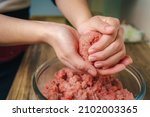 Close-up of a woman's hands preparing ground beef to make hamburgers, the meat is still raw and she is adding the ingredients, nice atmosphere in the kitchen.