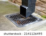 Small photo of Square black plastic drainage downpipe with a down spout shoe at the end of it. Fixed to a brick wall. Leading to a black plastic square gulley grid type drainage cover. Day outdoors. Close up.