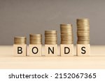 Bonds word in wooden blocks with coins stacked in increasing stacks. Bonds increasing concept. Copy space