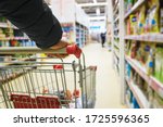 A man with a basket walks in a supermarket. Hand and part of the basket in focus, blurred background