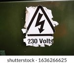 A warning sign which says danger of electrocution with 230 volts which is worn and peeling off