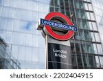 Small photo of Southwark, London, United Kingdom - August 29th 2022: Contemporary Underground Roundel on top of a sign for London Bridge station against a background of glass and steel modern office buildings