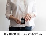 Small photo of Woman holding black dicey perfume bottle in her hands. Wearing white shirt.