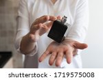 Small photo of Girl holding perfume on the palm of her hand. Small black dicey bottle with silver cap. Wearing white shirt.
