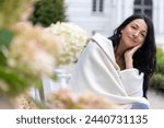 Small photo of A woman wrapped in a cream shawl sits amidst blooms, her content smile reflecting self-acceptance and grace at midlife amidst hormonal transition. High quality photo