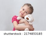 Happy child hugging teddy bear on white background caucasian little girl of 5-6 years in red looking at camera
