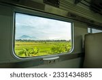 Small photo of Travel between cities by boarding an economy class train in Java, Indonesia, sitting by the window looking at the beautiful scenery outside the green rice fields that spoil the eyes of the passengers.