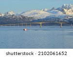 Red boat in front of Hadsel Bridge across the strait, at the back the snow-capped mountains of Hinnøya island, Langøysund, near Stokmarknes, Nordland, Vesteralen, Norway