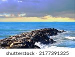 Small photo of Breakwater with waves in sea. Waves at the stone pier. A big wave in a storm breaks on the stones at pier. Wave splash on pier in sea. Waves crashing on breakwaters. Masonry breakwater in ocean.
