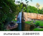 Waterfall in the African savannah. Waterfall from a large stone mountain among palm trees in the wild. Waterfall flowing down green hill in Jungle. Mountain river in tropical flowing over rocks.