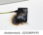 Small photo of Mobile phone after battery explosion. Smartphone burn. Mobile phone caught fire. Mobile smartphone overheat and catch fire. Cable overheat and catch fire. Smartphone burn, bang, blast, blowing up.