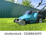 Small photo of Lawn Mower Electric for cutting grass in garden. Сutting grass in yard using Lawn Mower. Lawn mowing machine. Grass Trimmer and Grass Cutter. Lawn maintenance service. Gardener mows weeds