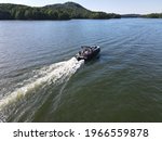 Pontoon boat cruising in open water on lake. Lake is surrounded by trees
