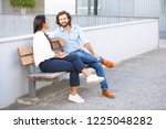 Attractive multiethnic businesspeople talking at sitting on bench near office building. Professional corporate couple on meeting in urban city. Teamwork concept