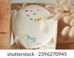 Small photo of Baby shower party cake with white cream cheese frosting decorated with blue and pink boy or girl text. Guess the gender of the upcoming child. He or She cake. Reveal the gender of the unborn baby.