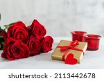 St. Valentine's Day present. Small hearts, candles, a gift box, and red roses bouquet on light background. Romantic love background. Happy Valentines Day. Greeting card, poster. Copy space for text