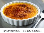 French Creme Brulee on the plate, with spoon on the side. On the marble table