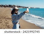 Small photo of a young girl takes a selfie on her phone on the seashore. happy girl calling via video chat on the seashore. A blogger girl takes a selfie on the seashore. sea holiday.