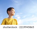 Child standing in profile blue sky with clouds on background. Boy 8 years old brunette, smiling face. Kid in yellow T-shirt. Concept of childhood, growing up, peace, dreams. Copy space. Sunny day.