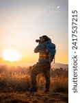Small photo of The photographer, camera in hand and backpack on his back, celebrates the encounter with the sun over the majestic mountains