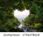 A heart-shaped hole in the dense tree crown. The current river to the cliff. The sun shines on the mountains. The concept of love for nature and passion for travel.