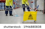 Small photo of Cropped shot of worker swearing safety overall holding mop cleaning floor in warehouse. Team of janitors with bucket washing floor in industrial storehouse