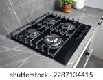 Contemporary black tempered glass gas stove hob with wok burner with auto ignition knob cast iron pan supports and flame safety valve built in compact high pressure laminate HPL countertop.