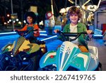 An African-American girl and a cute Caucasian boy riding a car ride together in the evening at a carousel and amusement park.