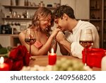 Happy Valentine's Day. A young couple in love with glasses of wine by candlelight sitting in the kitchen at the table, romantically spending the evening together.