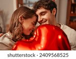 Happy Valentine's Day. Young couple in love holding a heart-shaped balloon while sitting on the sofa in the living room at home. Romantic evening together.