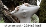 Small photo of wide banner panorama creepy halloween face of scary screaming woman in fear behind transparent fabric, cloth as ghost, specter between old tree trunks, copy space