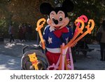Small photo of Madrid, Spain - Nov 09, 2021: A street performer dressed as Micky Mouse, poses with a child, making balloons to beg in the Retiro park